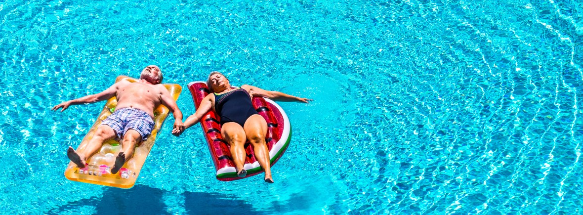 Total relax for happy mature senior retired people lay down on coloured lilos inflatable mattress on blue clear water of swimming pool in summer time - enjoying lifestyle and vacation